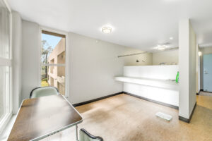 Interior laundry facilities, waiting table with 2 chairs, clothes hanging rack, folding table, white walls tile floors.