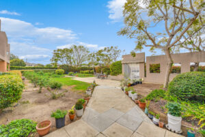 Exterior Courtyard, potted plants lining the sidewalk, gate leading to street, outdoor 3 4 seat tables arranged around the courtyard, high bushes privacy from street.