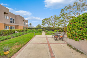 Exterior courtyard, 4 seat tables arranged around the courtyard, meticulous landscaping, high bushes meaning privacy from the street.