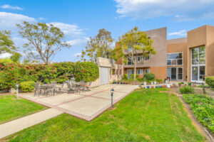 Exterior courtyard, 4 seat tables arranged around the courtyard, meticulous landscaping, high bushes meaning privacy from the street.