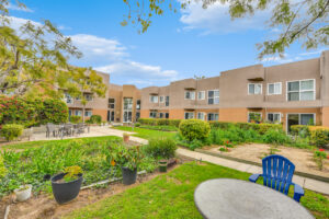 Exterior courtyard, 4 seat tables arranged around the courtyard, meticulous landscaping, high bushes meaning privacy from the street.