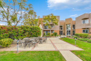 Exterior courtyard, 4 seat tables arranged around the courtyard, meticulous landscaping, high bushes meaning privacy from the street.