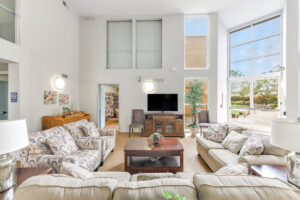 Interior Clubhouse/ leasing office lobby, 2 large couches, contemporary design, white walls, wood floors, 2 lounge chairs, multiple floral paintings, large windows along far-side wall.