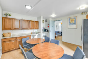 Interior Community kitchen, 2 tables 6 seats, wood floors, brown cabinetry, stainless steel appliances, laminate countertop.