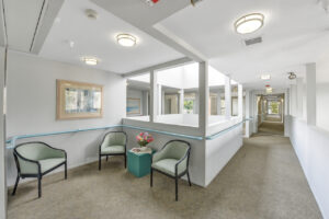Interior Upstairs hallway, white walls, 3 chairs, side table cube with flowers on top, gray carpeting.