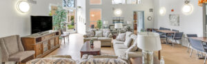 Interior Clubhouse/ leasing office lobby, 2 large couches, contemporary design, white walls, wood floors, 2 lounge chairs, multiple floral paintings, large windows along far-side wall.