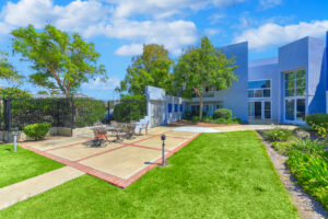Exterior courtyard, 4 seat tables arranged around the courtyard, meticulous landscaping, high bushes meaning privacy from the street.