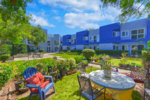 Exterior courtyard, 4 seat tables arranged around the courtyard, meticulous landscaping, high bushes meaning privacy from the street.