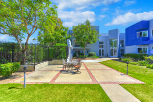 Exterior courtyard, 4 seat tables arranged around the courtyard, meticulous landscaping, high bushes meaning privacy from the street.
