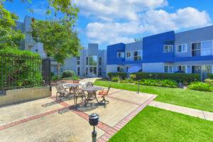 Exterior courtyard, 4 seat tables arranged around the courtyard, meticulous landscaping, high bushes meaning privacy from the street.