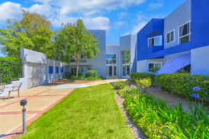 Exterior courtyard, 4 seat tables arranged around the courtyard, meticulous landscaping, high bushes meaning privacy from the street.