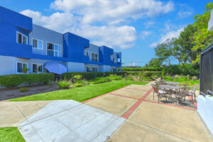 Exterior courtyard, 4 seat tables arranged around the courtyard, meticulous landscaping, high bushes meaning privacy from the street.